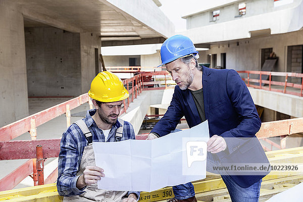 Bauarbeiter und Architekt mit Plangespräch auf der Baustelle