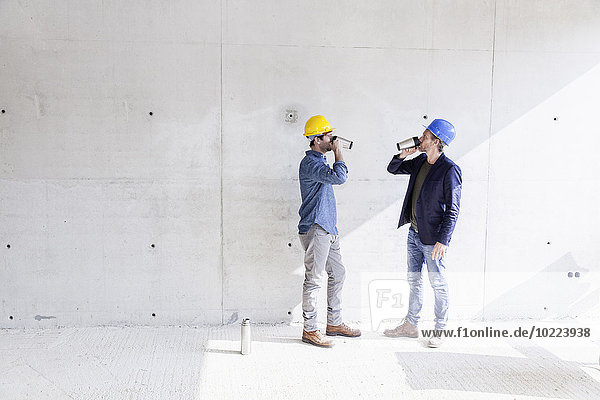 Zwei Männer auf der Baustelle trinken aus Tassen.