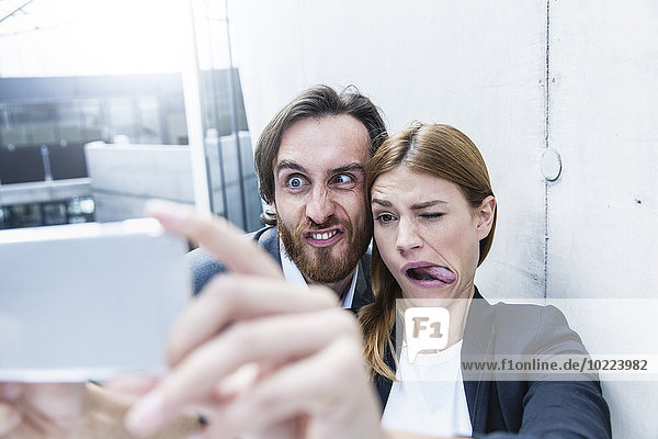 Porträt von zwei Geschäftsleuten  die Gesichter machen  während sie einen Selfie mit dem Smartphone nehmen.