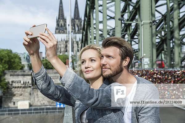 Germany  Cologne  young couple taking a selfie with smartphone at Hohenzollern Bridge