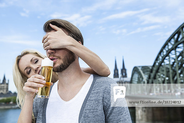 Germany  Cologne  young man tasting Koelsch while his girlfriend covering his eyes