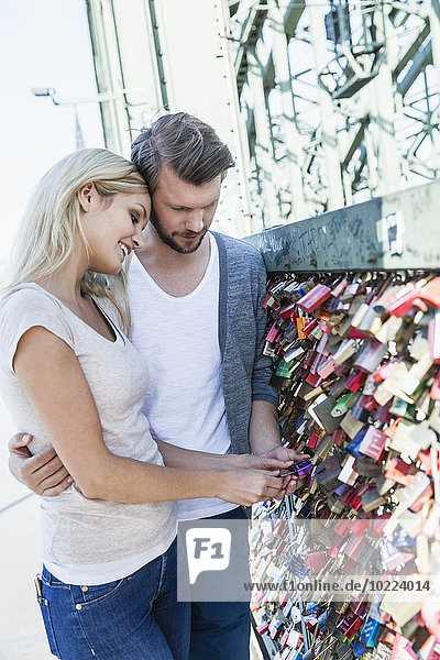 Germany  Cologne  young couple looking at love locks on Hohenzollern Bridge