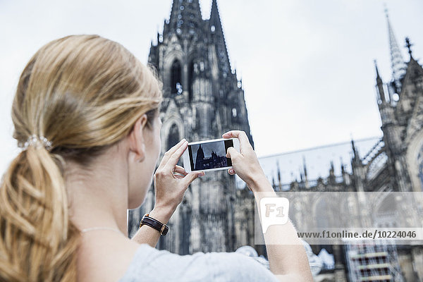 Deutschland  Köln  junge Frau beim Fotografieren des Kölner Doms mit Smartphone