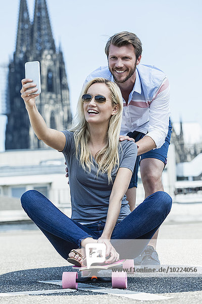 Germany  Cologne  portrait of smiling young couple taking a selfie with smartphone