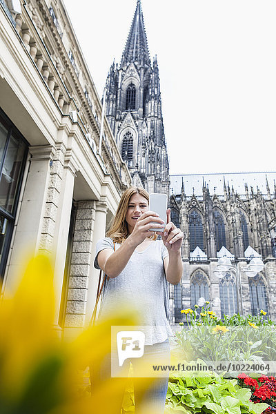 Deutschland  Köln  junge Frau mit einem Selfie mit Smartphone vor dem Kölner Dom