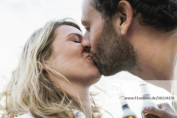 Paar mit Bierflaschen  die sich im Freien küssen.