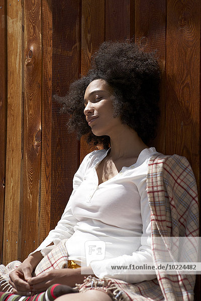 Sunbathing young woman leaning on wooden wall