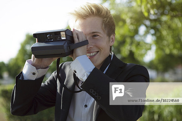 Smiling young man outdoors taking picture with polaroid camera