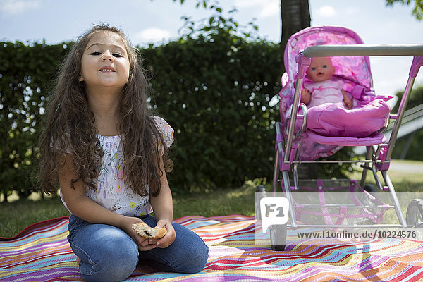 Kleines Mädchen sitzend auf einer Decke neben ihrem Puppenwagen