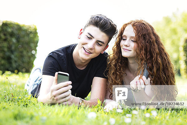 Teenager-Paar auf einer Wiese liegend mit Blick auf Smartphone