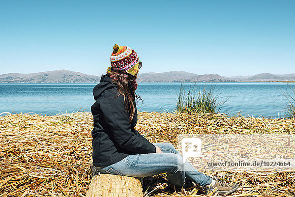 Peru  Puno  woman wearing chullo sitting on floating island in Lake Titicaca