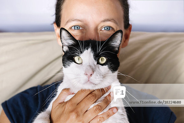 Blauäugige Frau  die eine schwarz-weiße Katze hält.