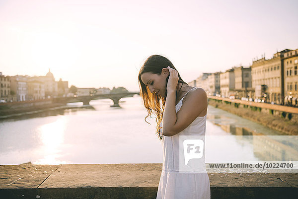 Italien  Florenz  glückliche Frau in weißem Sommerkleid auf einer Brücke stehend bei Sonnenuntergang