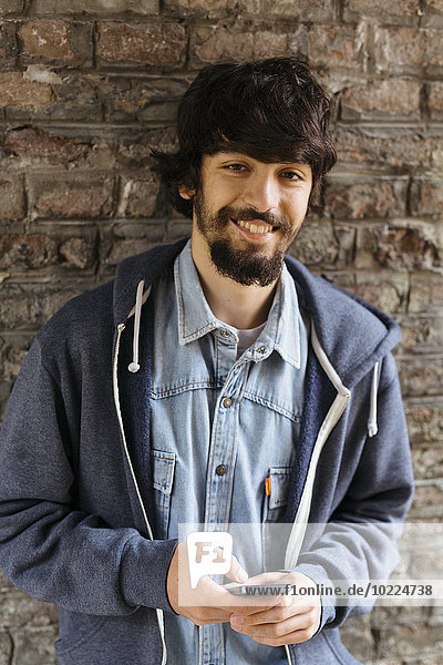 Porträt eines lächelnden jungen Mannes mit Smartphone