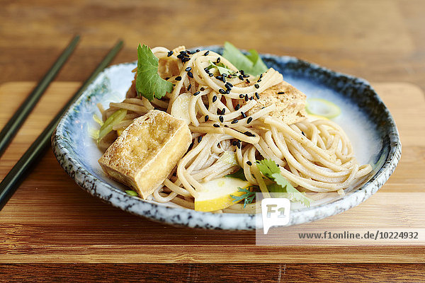 Asiatischer Nudelsalat mit Sobanudeln  Tofu  grünen Zwiebeln  gelben Zucchini und Koriander  garniert mit schwarzen Sesamsamen