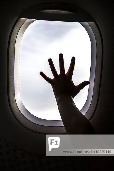 Silhouette der Mädchenhand am Fenster eines Flugzeuges