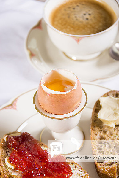 Frühstückstisch mit schwarzem Kaffee  gekochtem Ei und Brot mit Marmelade