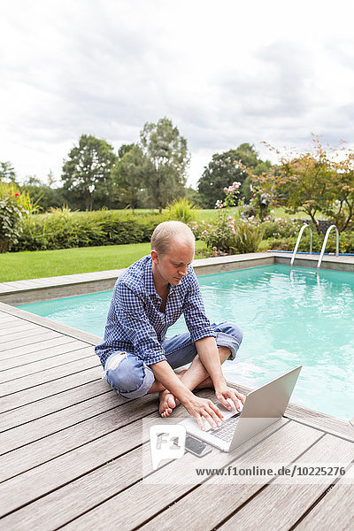 Man sitting on floor beside a pool using laptop