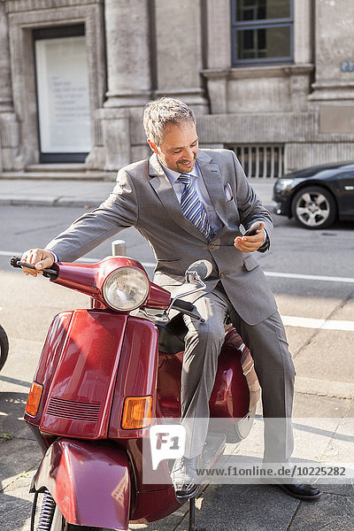 Deutschland  Stuttgart  lächelnder Geschäftsmann auf Motorroller sitzend