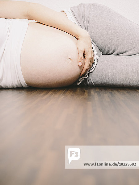Schwangere Frau  die auf einem Holzboden ruht und ihren Bauch hält.