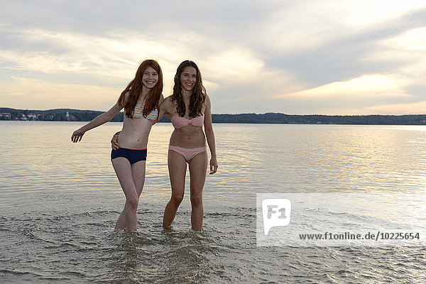 Germany  Upper Bavaria  two girls wading arm in arm in the water of Lake Starnberg