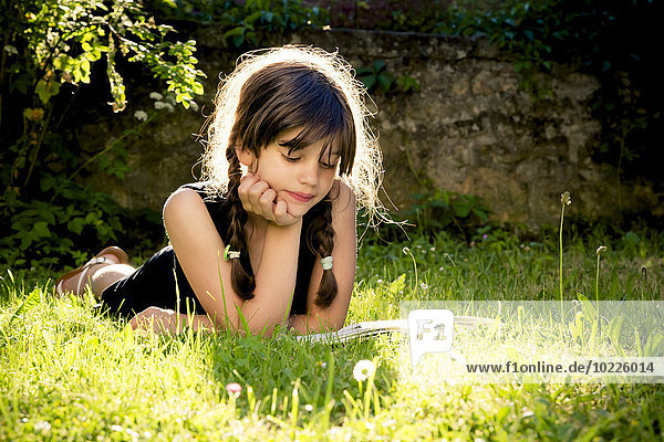 Girl lying on a meadow reading a book
