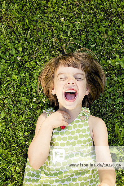 Little girl with open mouth and closed eyes lying on a meadow