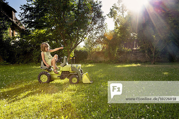 Kleines Mädchen spielt mit Spielzeugtraktor im Garten