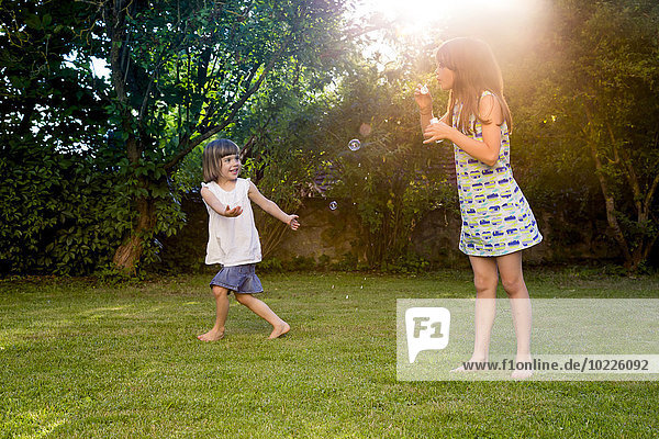 Zwei Schwestern beim Spielen mit Seifenblasen im Garten