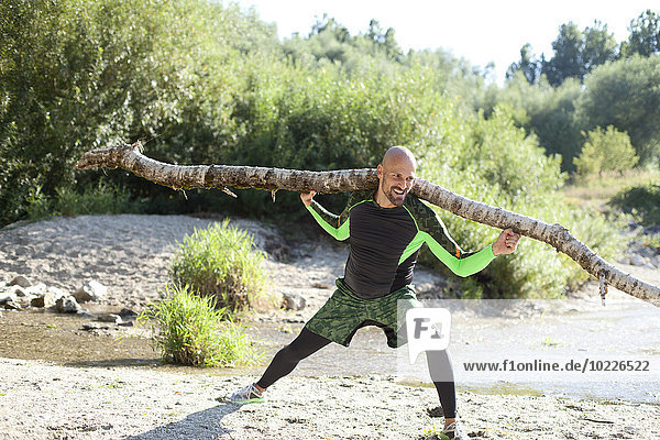 Man doing CrossFit exercise with tree trunk on his shoulders