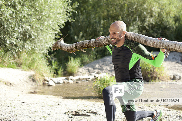 Man doing CrossFit exercise with tree trunk on his shoulders