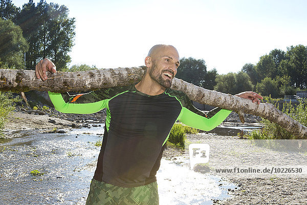 Smiling man doing CrossFit exercise with tree trunk on his shoulders
