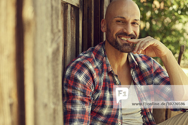 Portrait of smiling man wearing checked shirt sitting in front of wooden hut