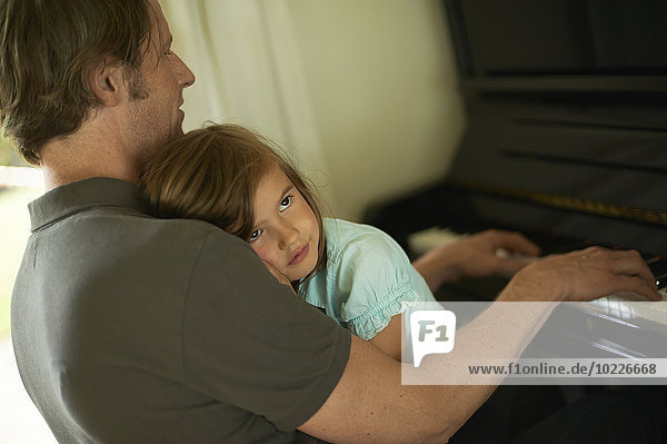 Vater spielt Klavier mit Tochter auf dem Schoß