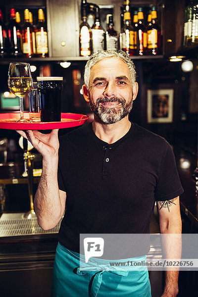 Portrait of smiling waiter holding tray with beverages in an Irish pub