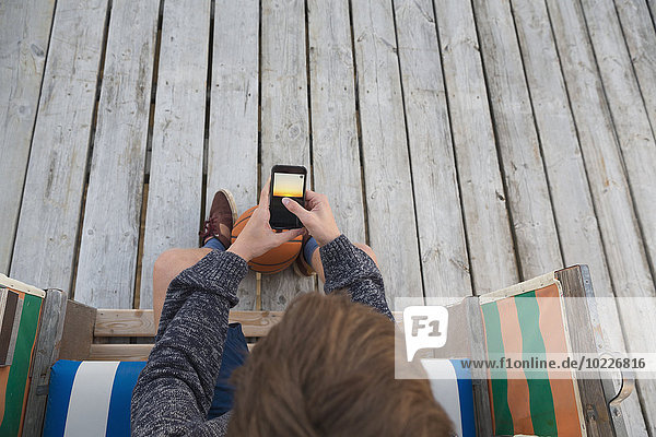 Teenager-Junge mit Basketball und Smartphone im Strandkorb sitzend