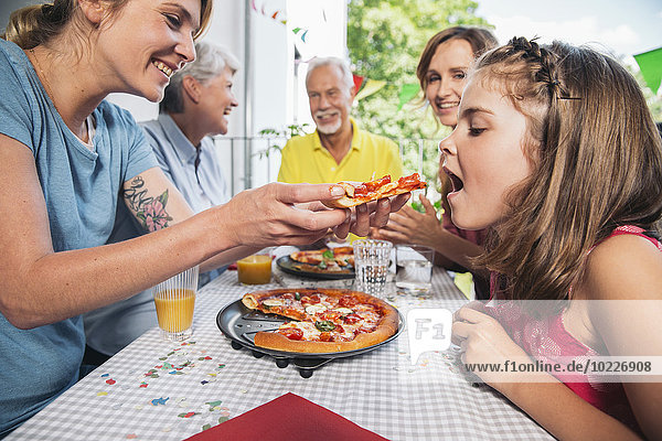 Girl being fed with homemade pizza at family party