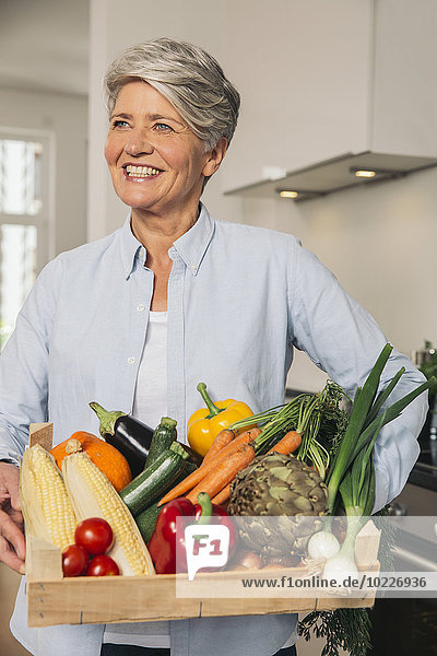 Portrait of woman holding wooden box of vegetables