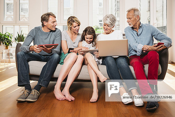 Group picture of three generations family with different digital devices sitting on one couch