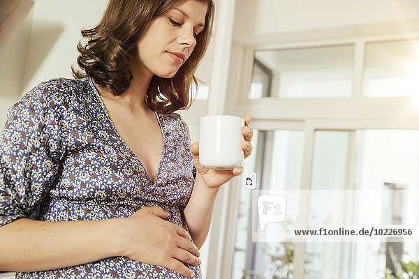 Schwangere Frau mit einer Tasse Tee  die ihren Bauch hält.