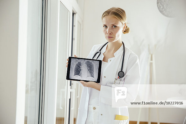 Portrait of serious female doctor showing an x-ray on digital tablet
