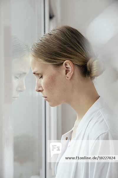 Exhausted female doctor leaning against window with eyes closed