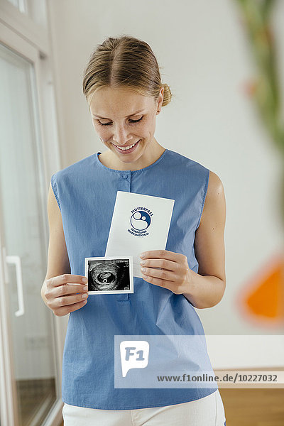 Smiling young woman holding ultrasound image and maternity log