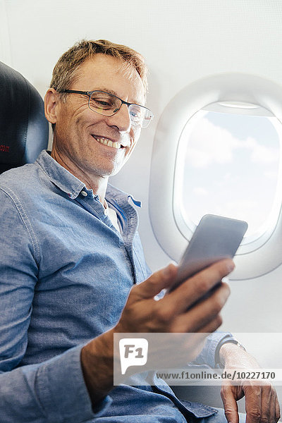 Ein reifer Mann sitzt in einem Flugzeug und schaut auf sein Smartphone.