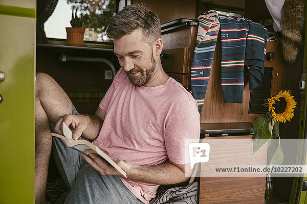 Lächelnder Mann beim Lesen eines Buches im Van