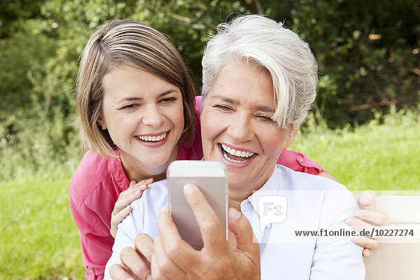 Lachende Mutter mit erwachsener Tochter beim Blick auf das Handy im Freien