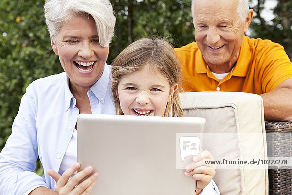 Glückliche Großeltern und Mädchen im Freien mit digitalem Tablett