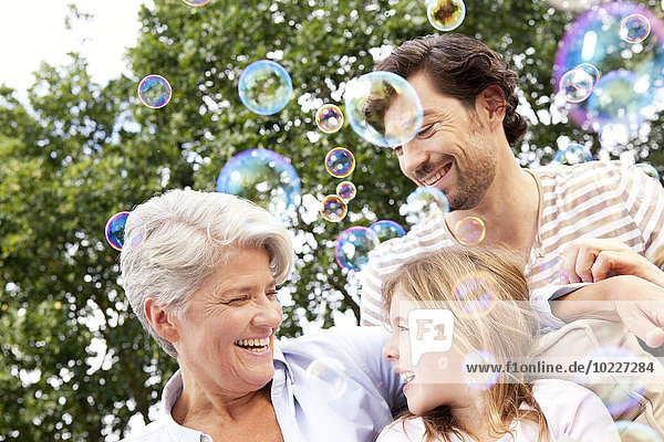 Glückliche Großmutter,  Vater und Mädchen umgeben von Seifenblasen