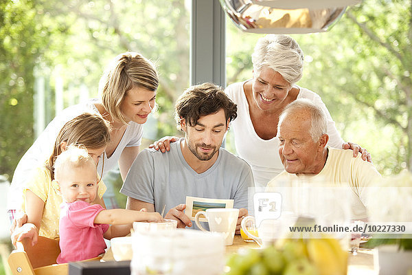 Vater mit seiner Familie beim Lesen der Postkarte am Frühstückstisch