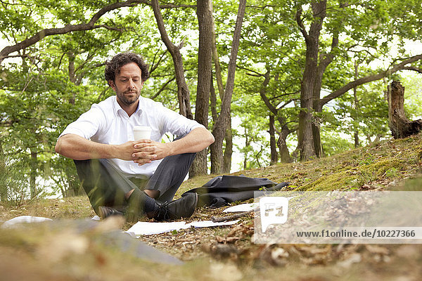 Deutschland  Geschäftsmann im Wald sitzend mit Kaffee zum Mitnehmen
